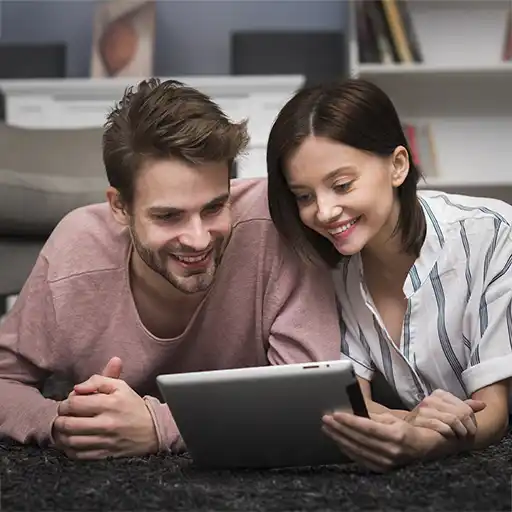 Smiling young couple lying on a carpet and looking at a tablet together in a cozy living room.